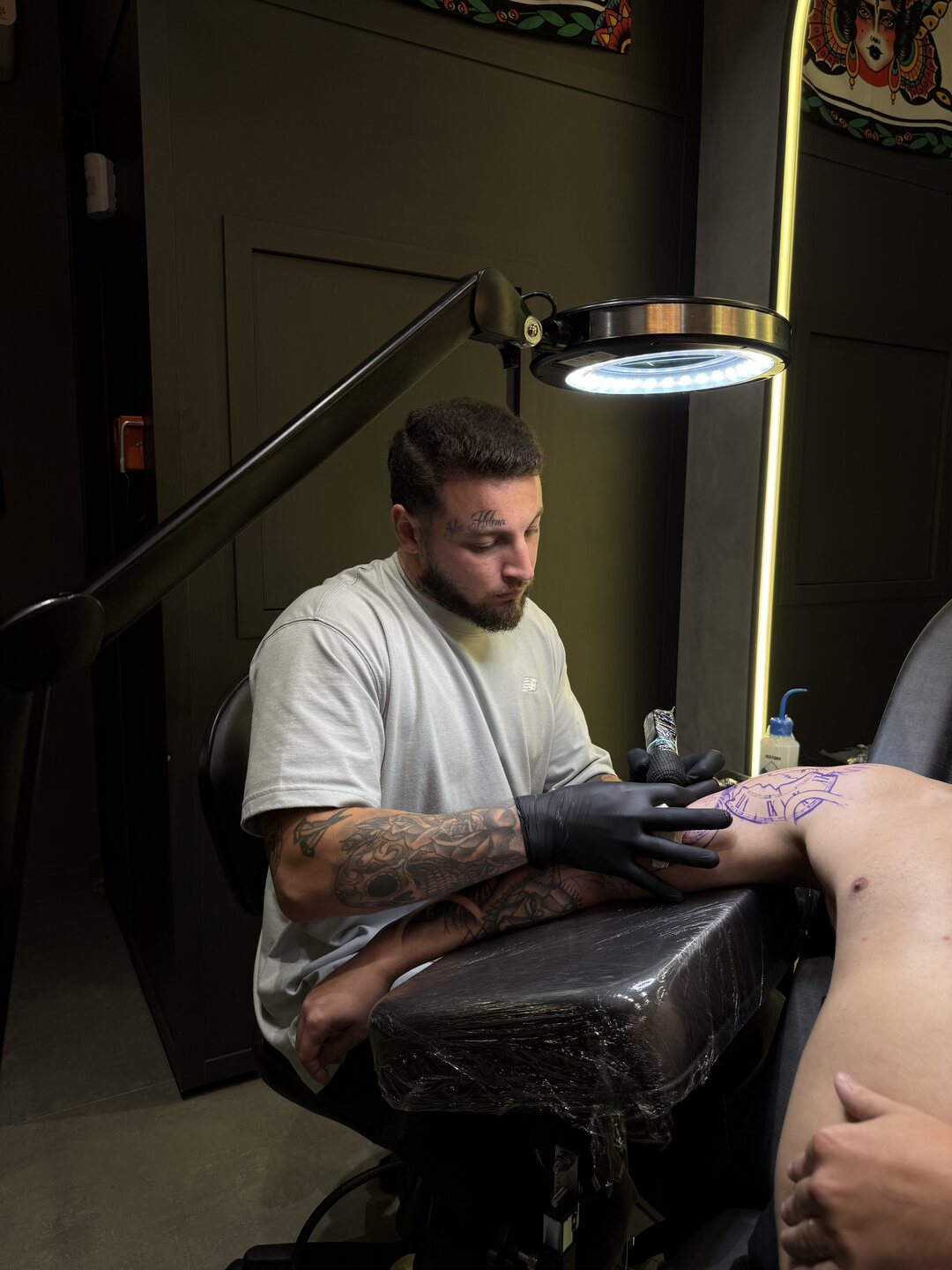 Rômulo Murillo, de luvas pretas, tatuando um braço no estúdio